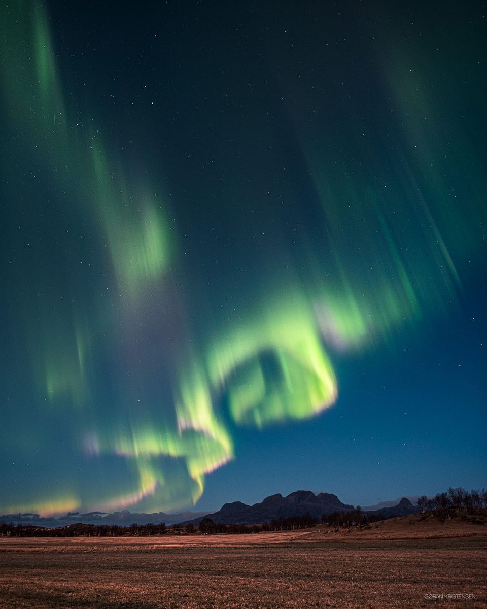 Nordlys i grønt over et jorde, med et lite fjell i bakgrunnen