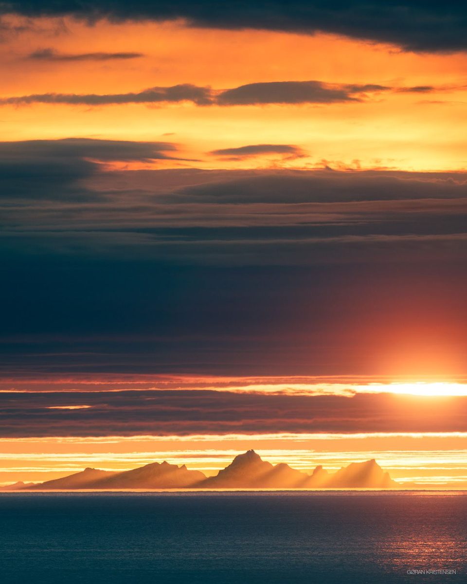 Solnedgang med en øysilhuett i horisonten, gyllent lys