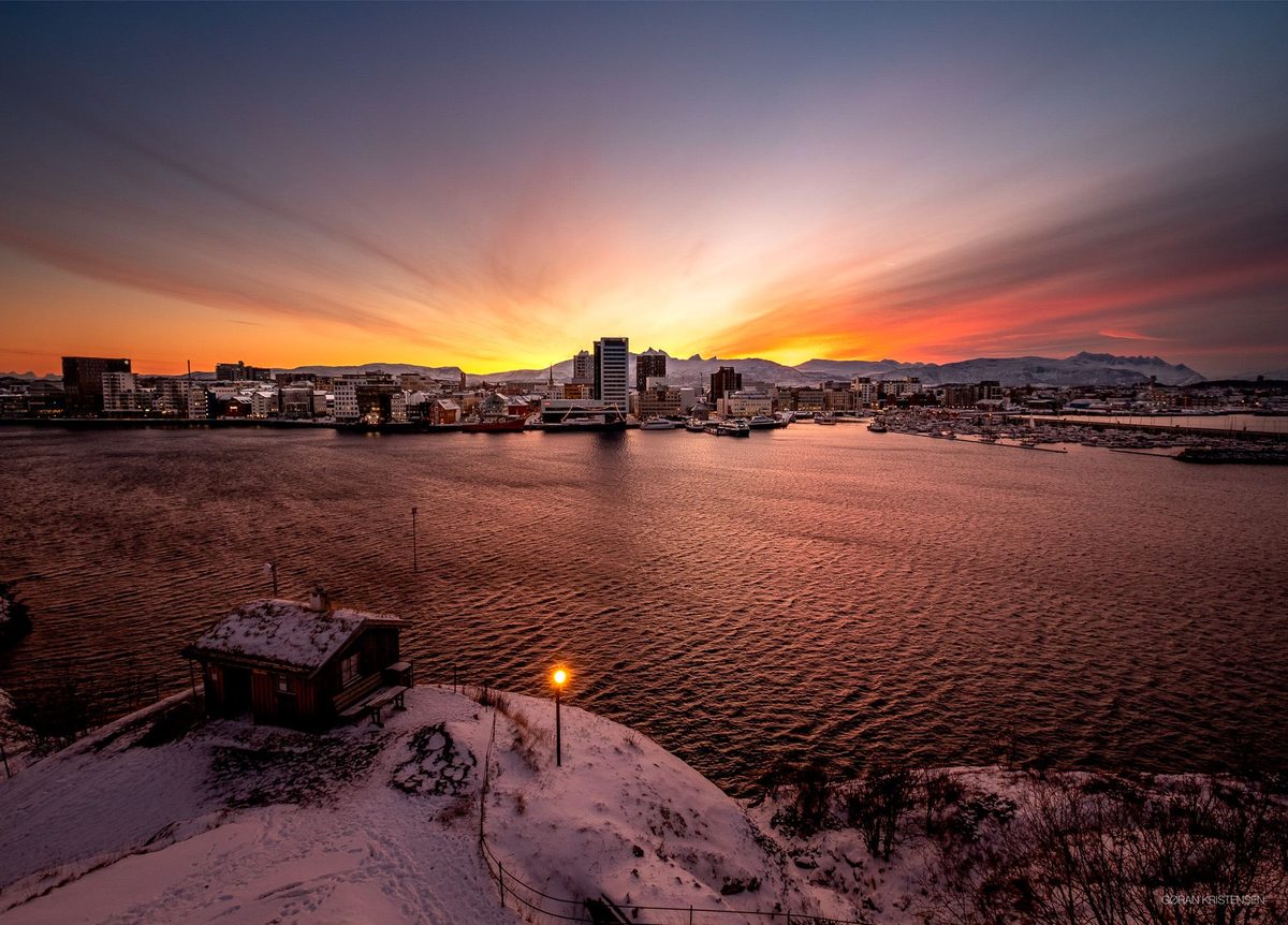 Bylys ved solnedgang, med en liten hytte i forgrunnen og fargerik himmel