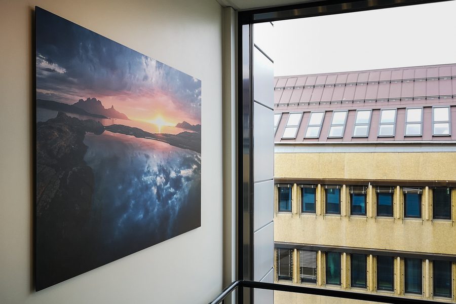 Stort fotografi på aluminium montert på en vegg i en trappeoppgang, med utsikt gjennom et vindu ved siden av